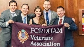 A group of people are holding a fordham veterans association flag.