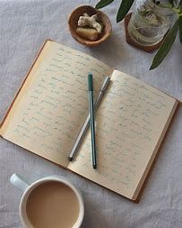 A notebook with two pens and a cup of coffee on a table.