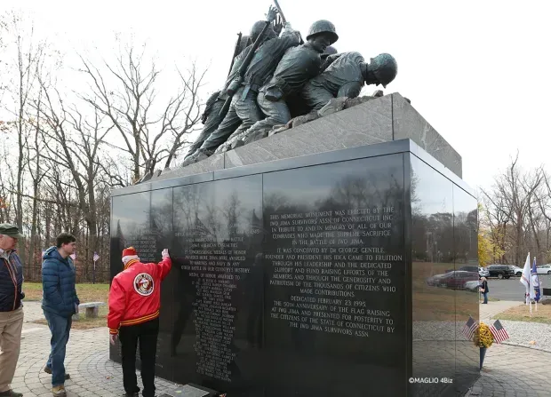 A man in a red jacket stands in front of a iwo jima statue in newington, ct