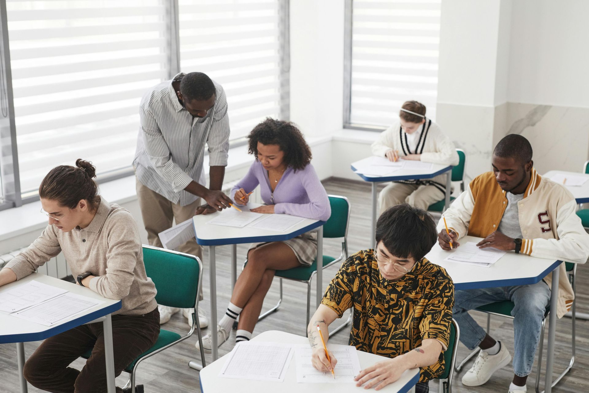 Students taking a written exam in a bright classroom, seated at individual desks.