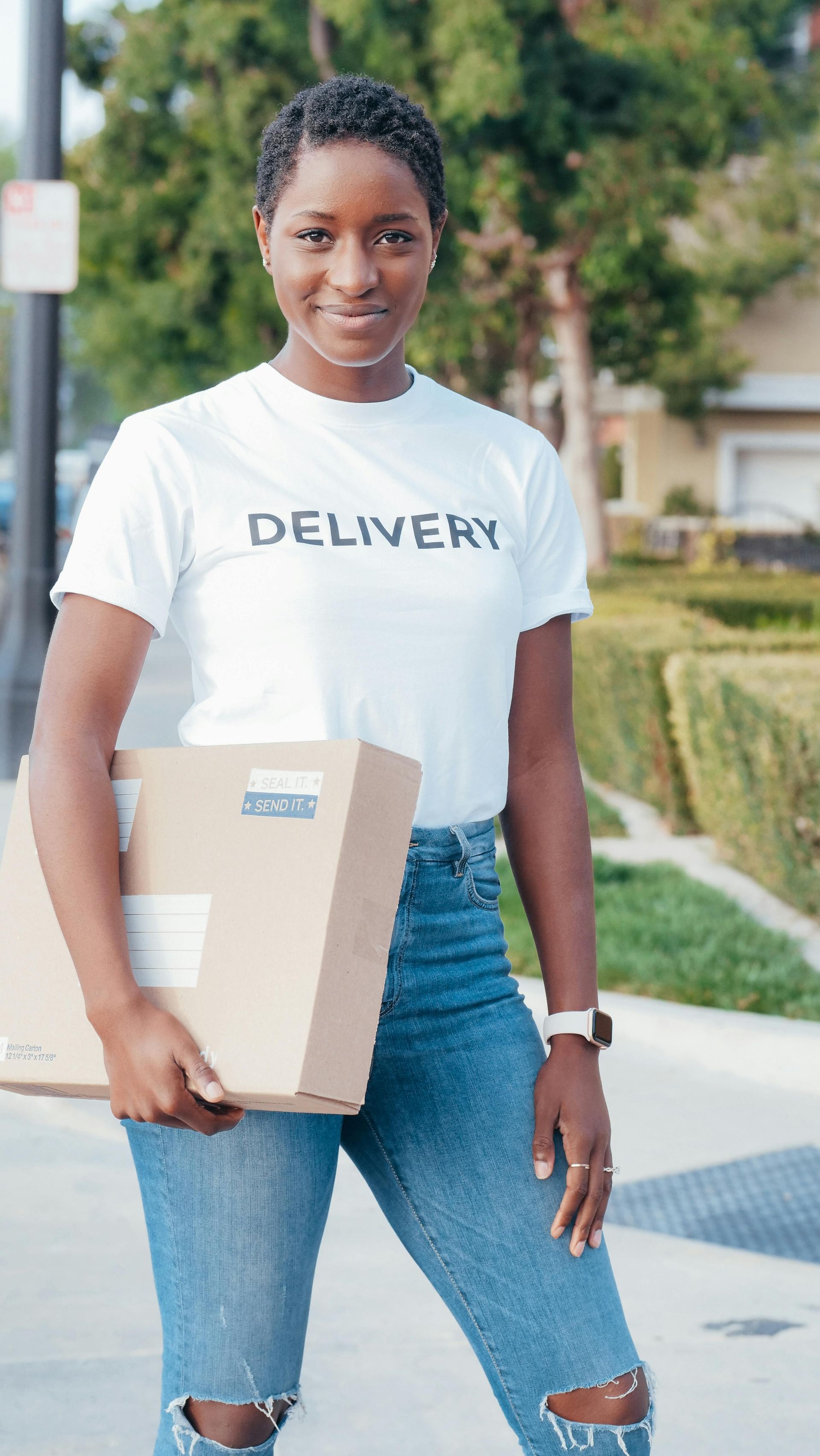 A woman in a delivery t-shirt is holding a cardboard box.