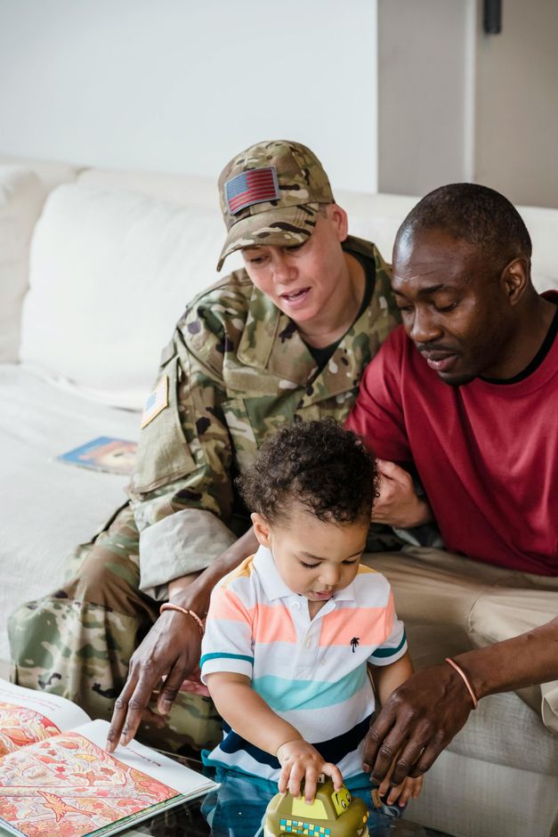 Two adults and a toddler playing together on a couch, with toys and a wrapped gift nearby.