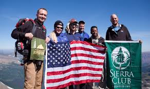 A group of people are standing on top of a mountain holding american flags.