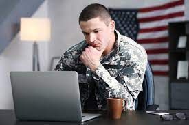 A soldier is sitting at a desk using a laptop computer.