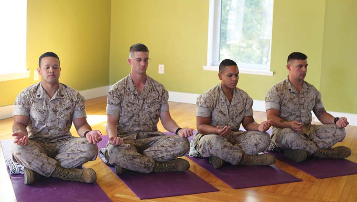 A group of soldiers are sitting on yoga mats in a room.