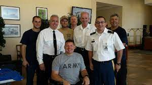 A group of men standing around a man in an army shirt.