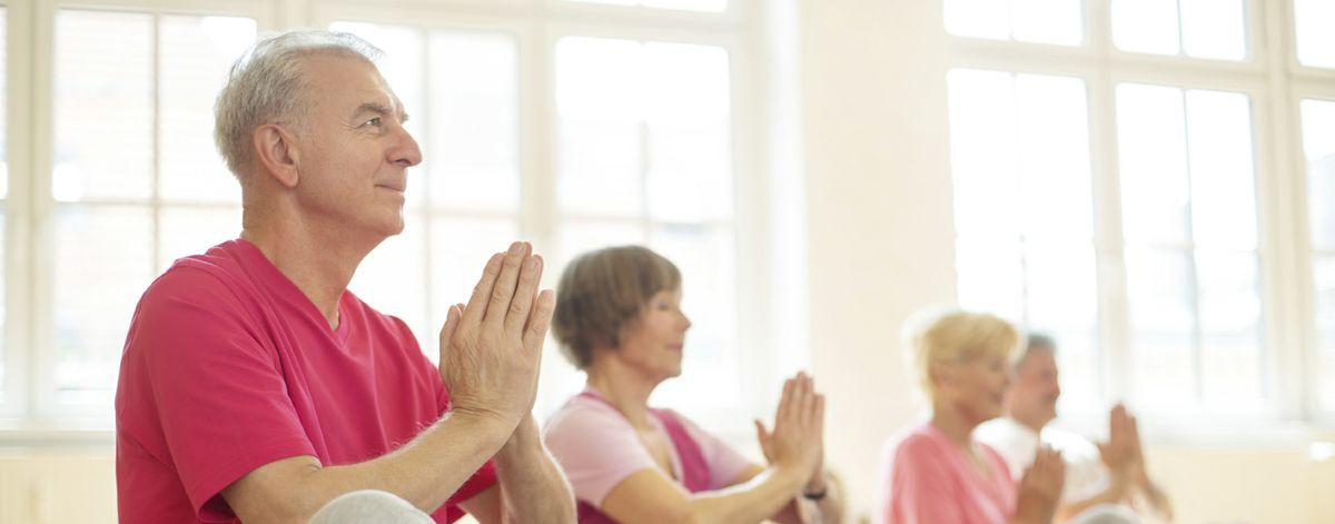 People seated in a bright room practicing yoga or meditation, hands together in a prayer pose