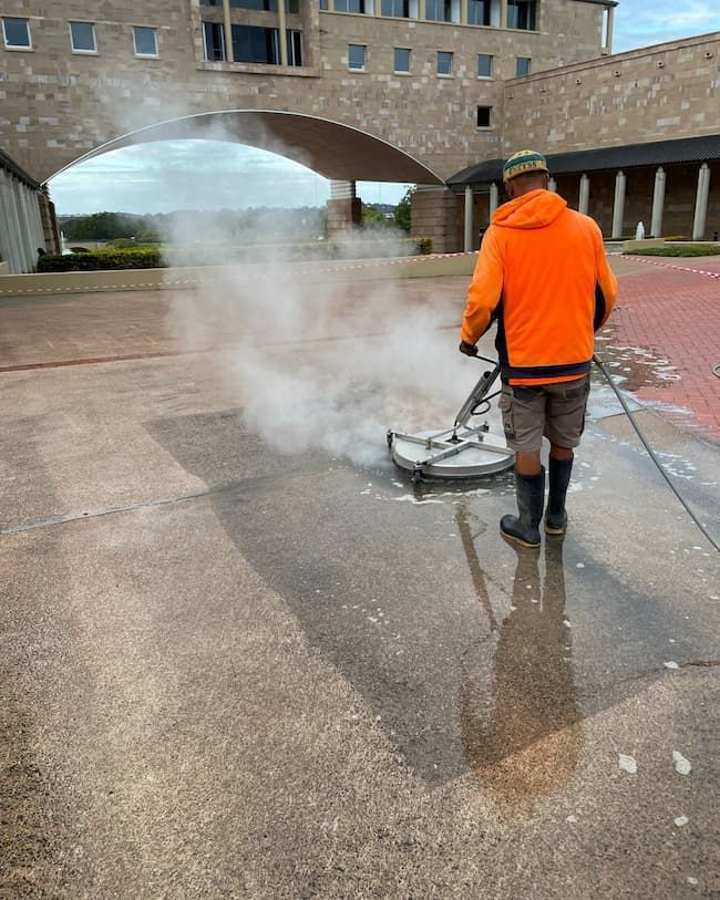 A Man is Using a Machine to Clean a Concrete Driveway — Excess Cleaning in Robina, QLD
