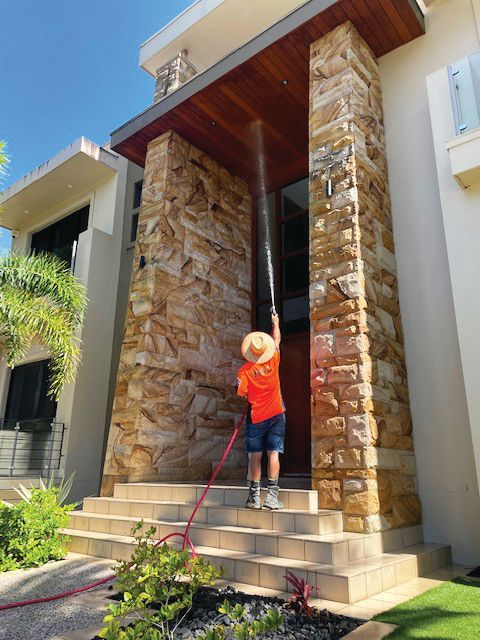A Man is Spraying Water on the House — Excess Cleaning in Molendinar, QLD