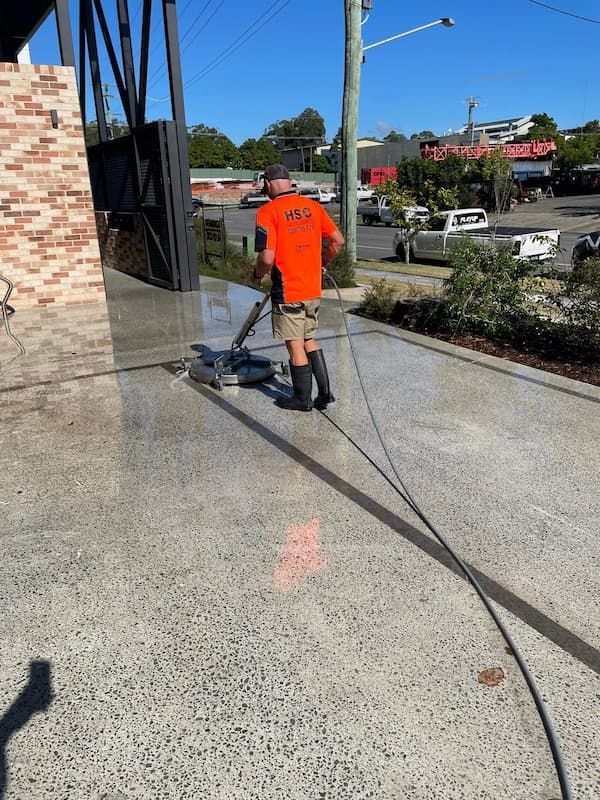 Man With a Hose Spraying the Side of a Building — Excess Cleaning in Molendinar, QLD