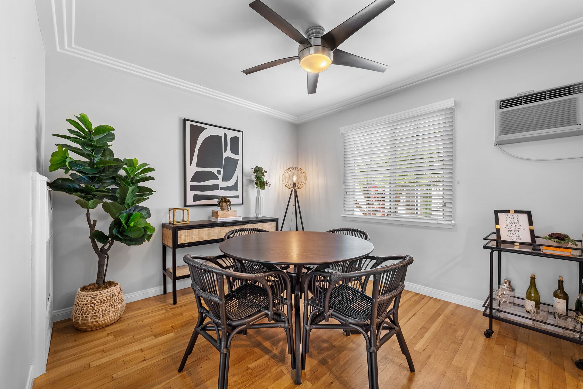 Dining room with a round table, chairs, and a tall plant next to a sideboard.