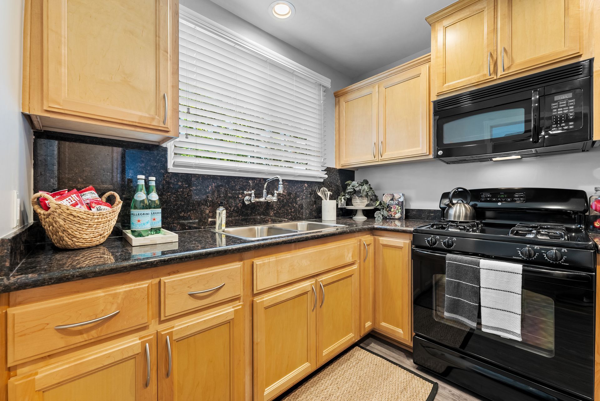 Kitchen with light wood cabinets, black appliances, and dark countertops.