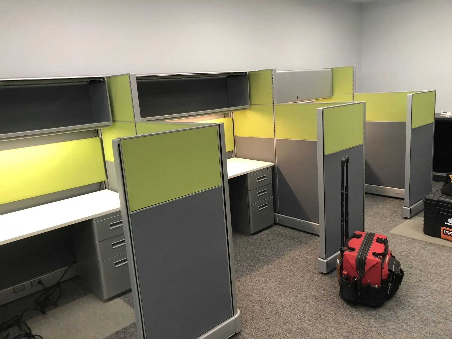 A row of cubicles in an office with a red bag on the floor.