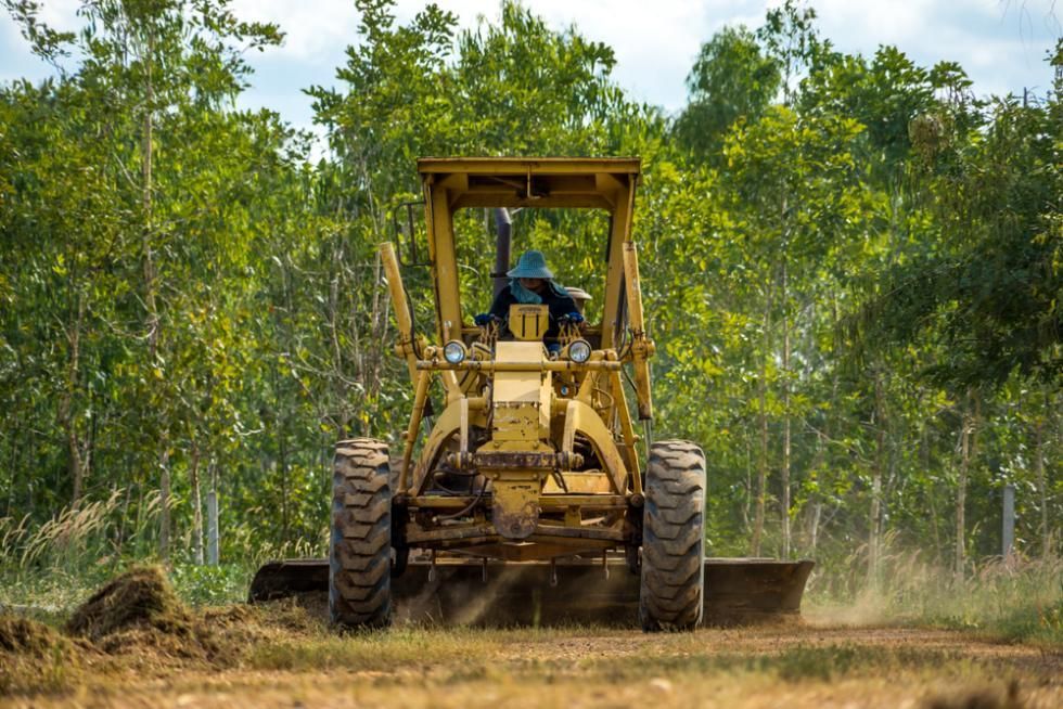 A Man is Driving a Bulldozer on a Dirt Road — SMH Valley Fencing & Maintenance In Millfield, NSW