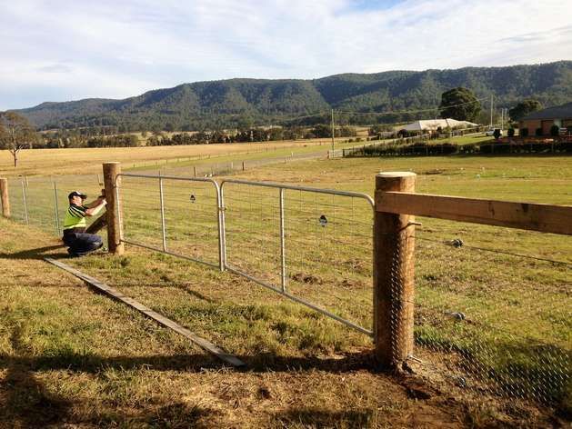 A Man Building Wire Fence with Wooden Posts— SMH Valley Fencing & Maintenance In Millfield, NSW