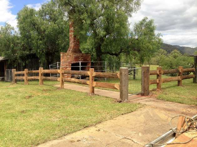 A Wooden Fence Surrounds a Grassy Field With a Brick Fireplace — SMH Valley Fencing & Maintenance In Millfield, NSW