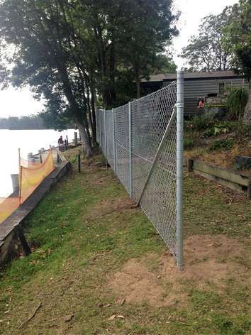 A Chain Link Fence Surrounds a Grassy Area Next to a Body of Water — SMH Valley Fencing & Maintenance In Millfield, NSW