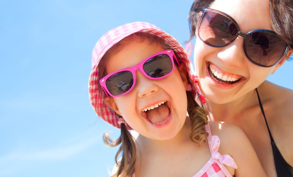 A Woman And A Little Girl Wearing Sunglasses And Hats Are Smiling For The Camera — Regal's Dental In Yeppoon, QLD