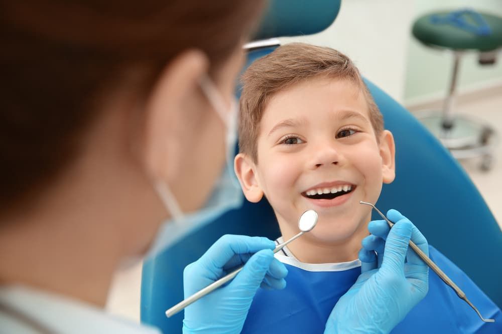 A Young Boy Is Sitting In A Dental Chair While A Dentist Examines His Teeth — Regal's Dental In Yeppoon, QLD