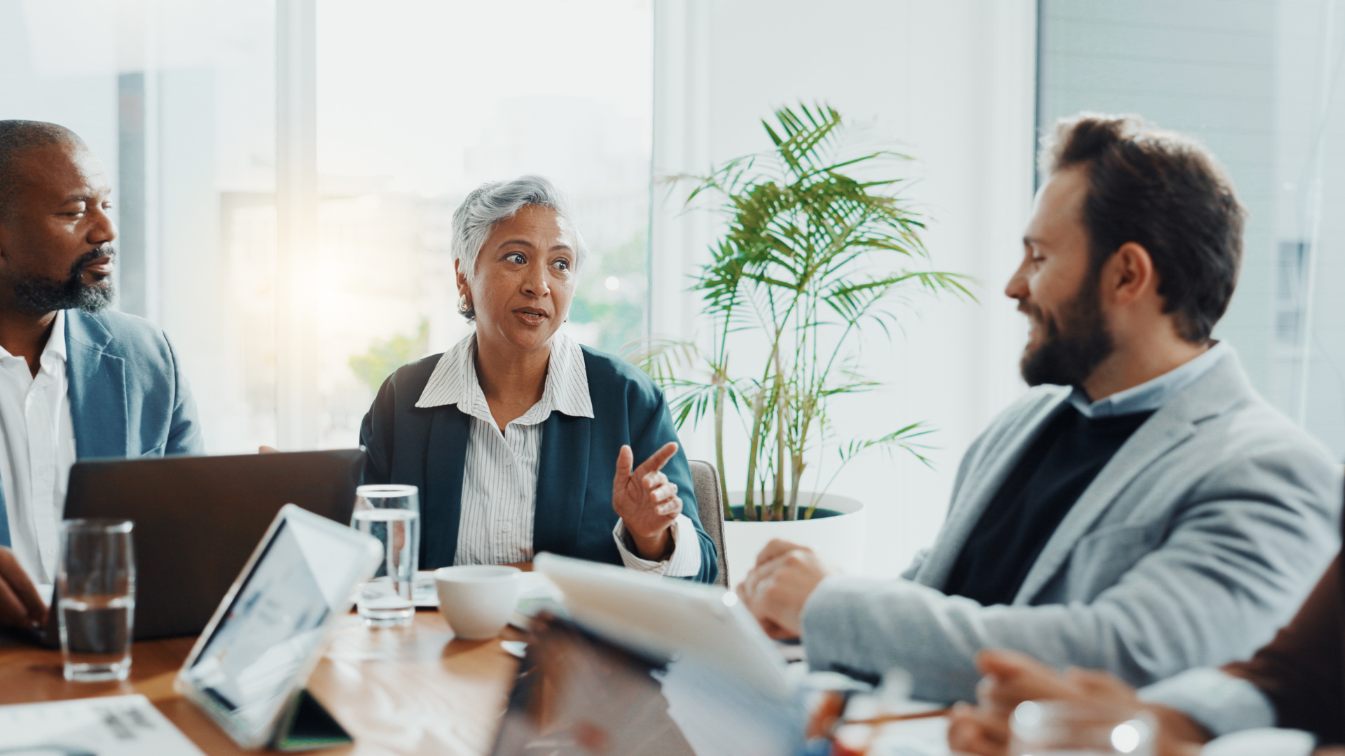 A diverse group in a meeting. A woman speaks animatedly. Light-filled, modern office.