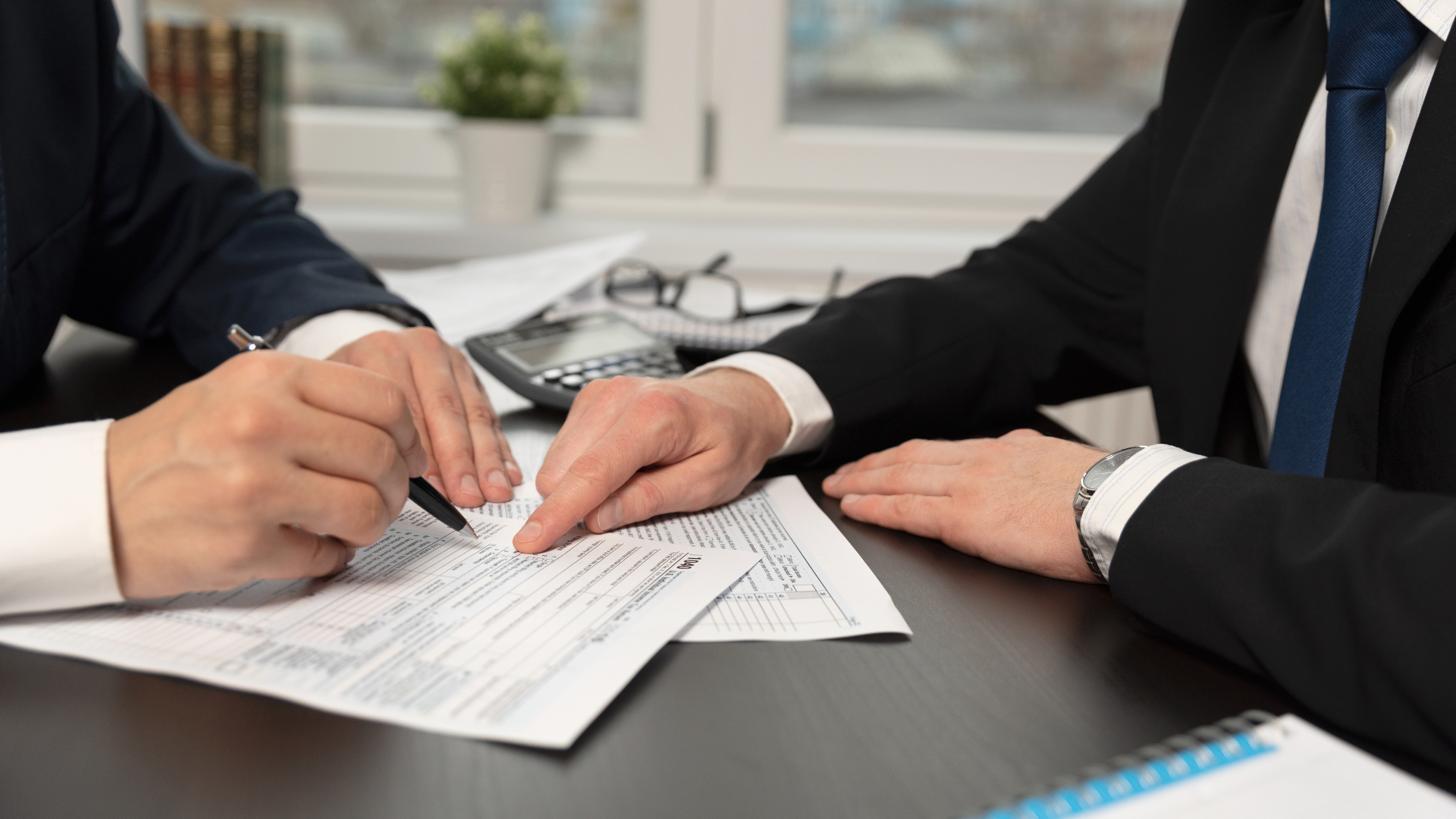 Two businesspeople reviewing paperwork, one pointing, the other writing with a pen.