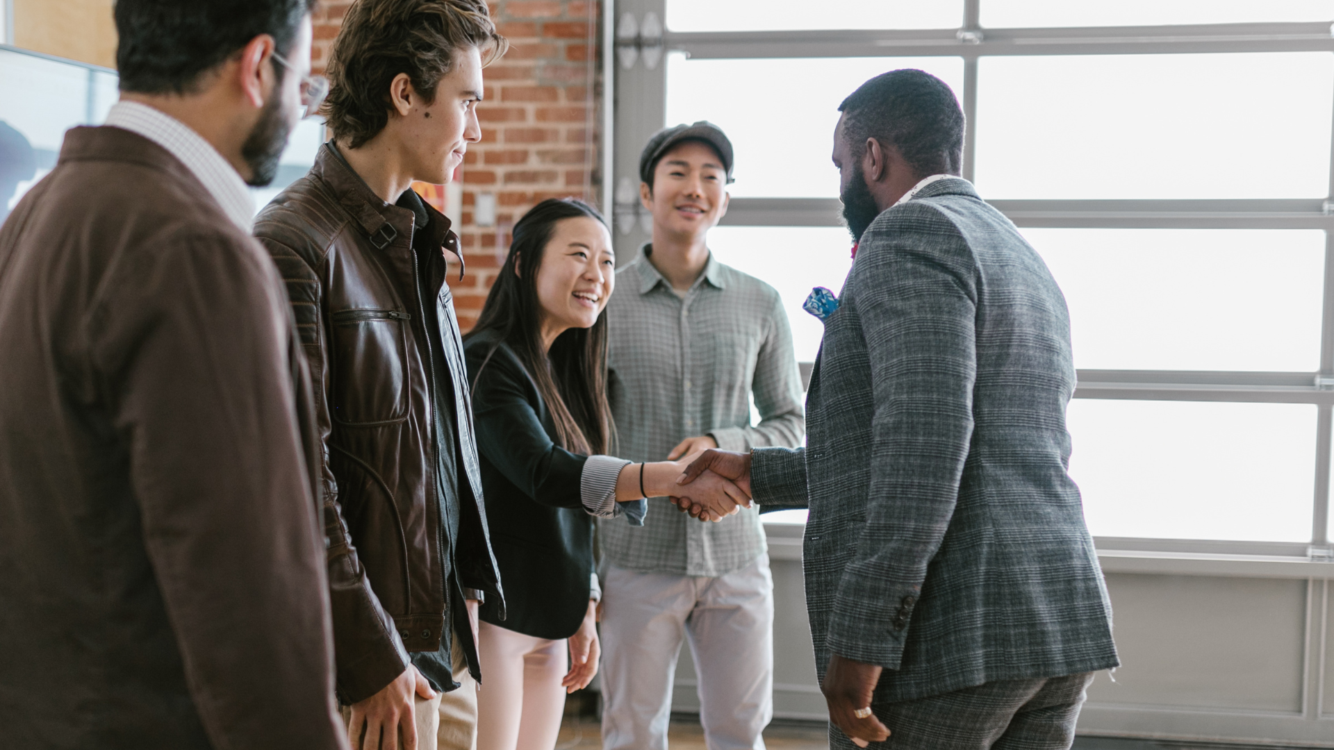 Group of people greeting each other in an office setting; handshake between a woman and a man.