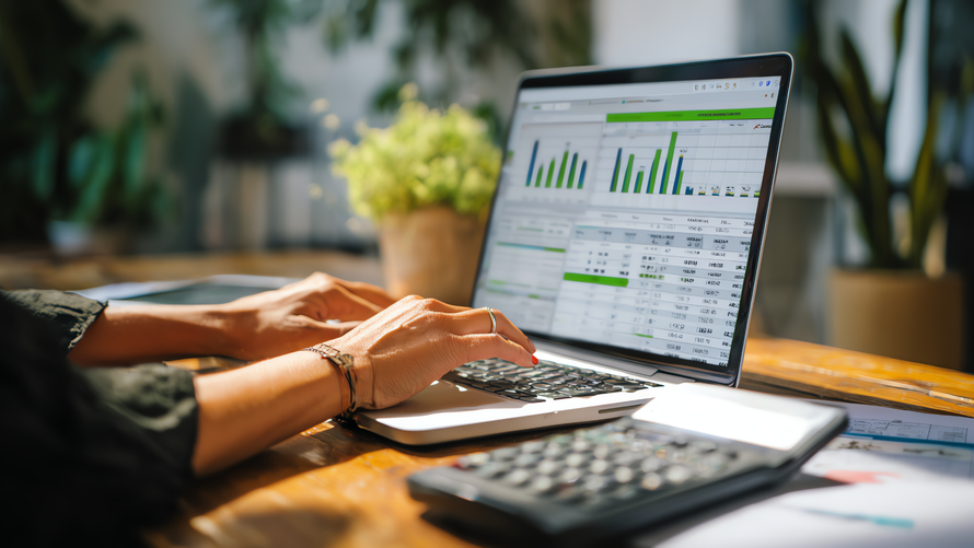 Person working on laptop with charts and calculator on desk.