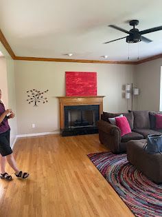 A woman is standing in a living room with a fireplace and a ceiling fan.