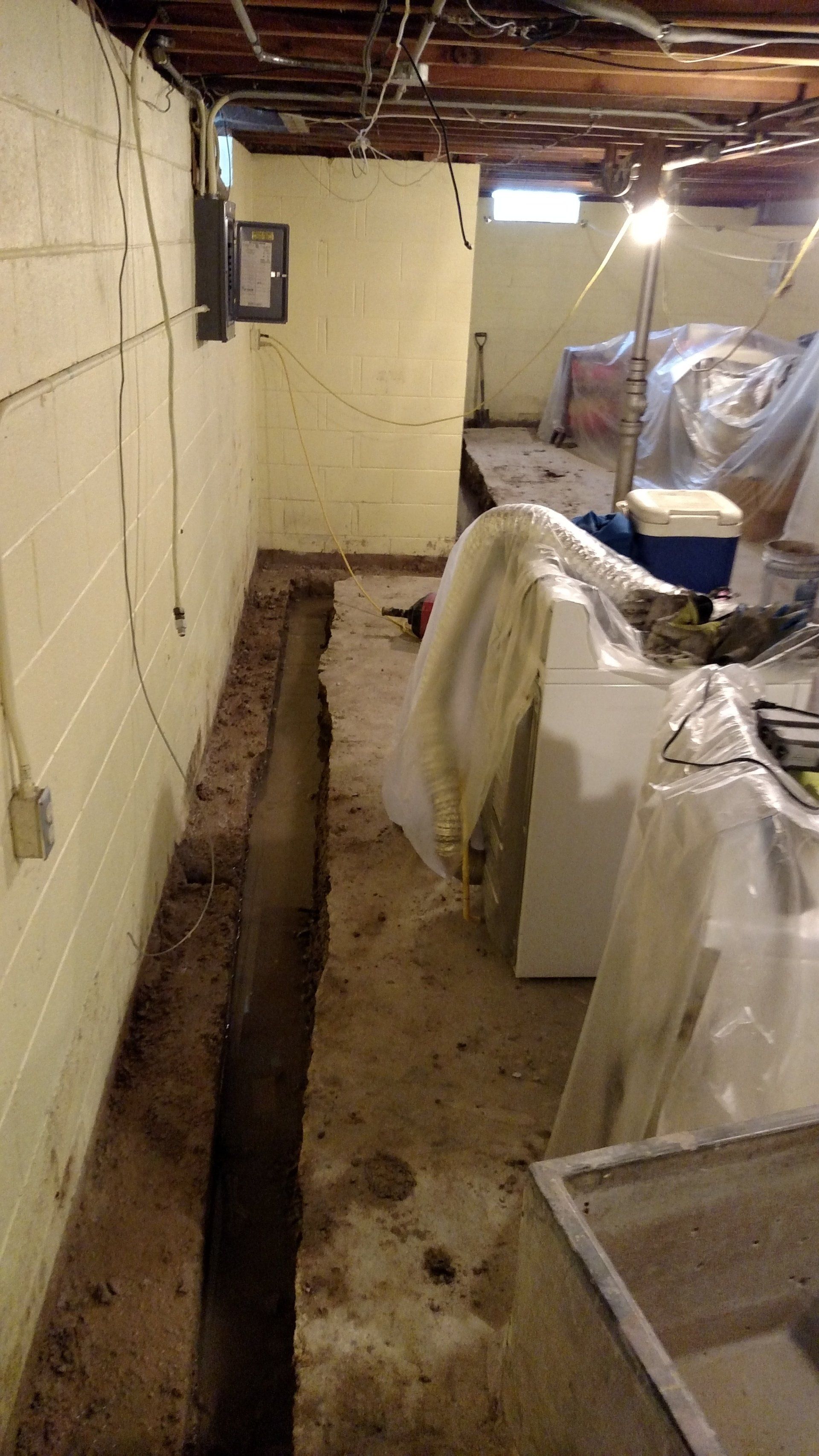 A basement with a hole in the floor and a few appliances in it.