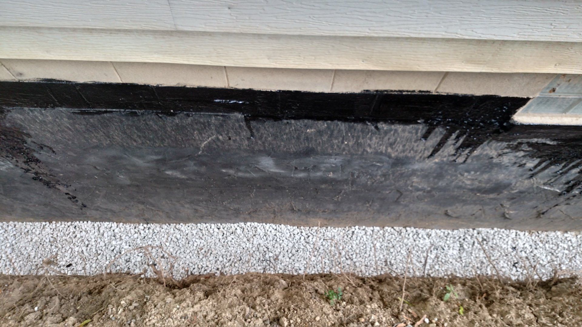 exterior basement waterproofing A black sheet of plastic is sitting on the ground next to a house.