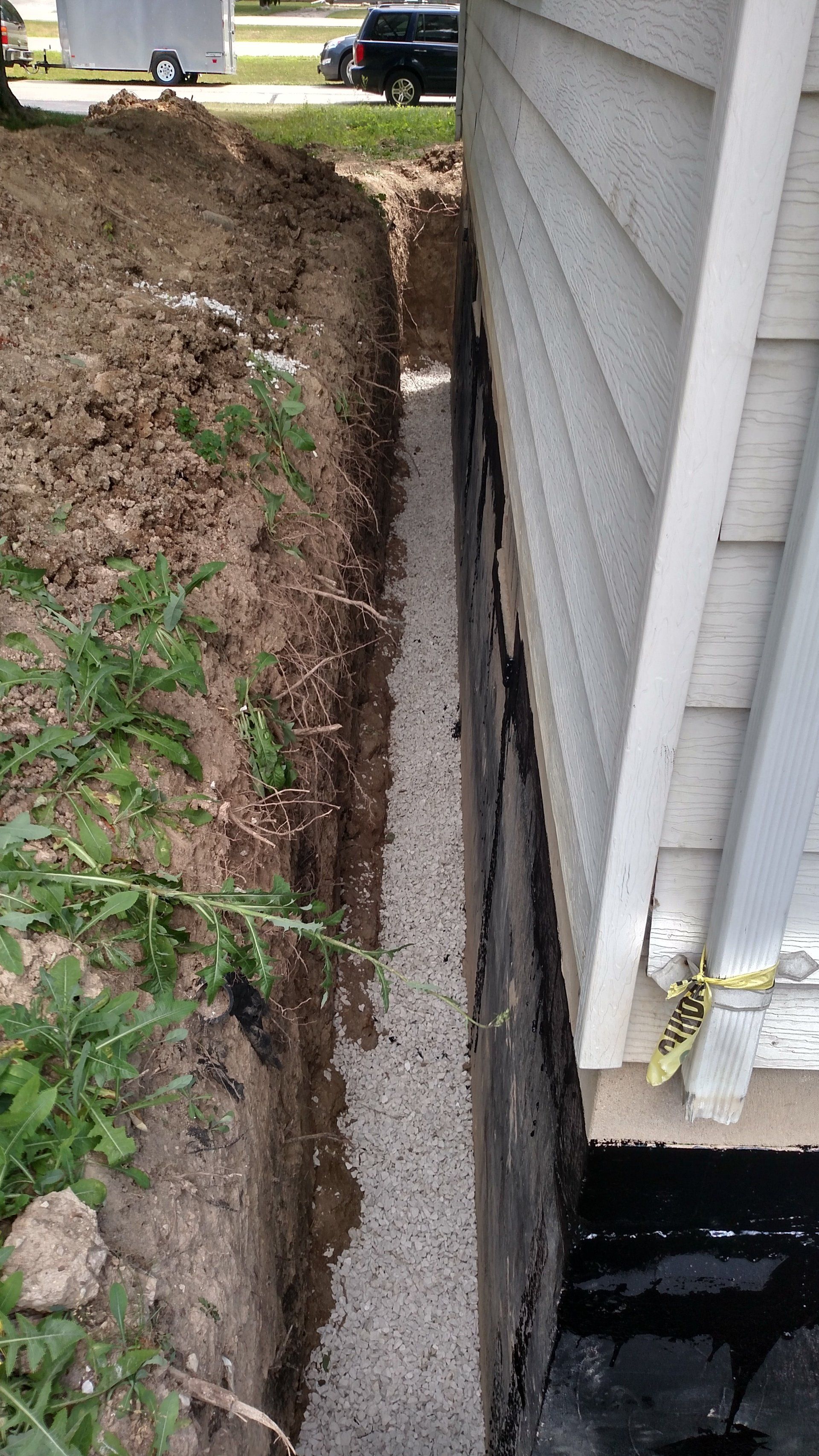 exterior waterproofing A drainage system is being installed on the side of a house.