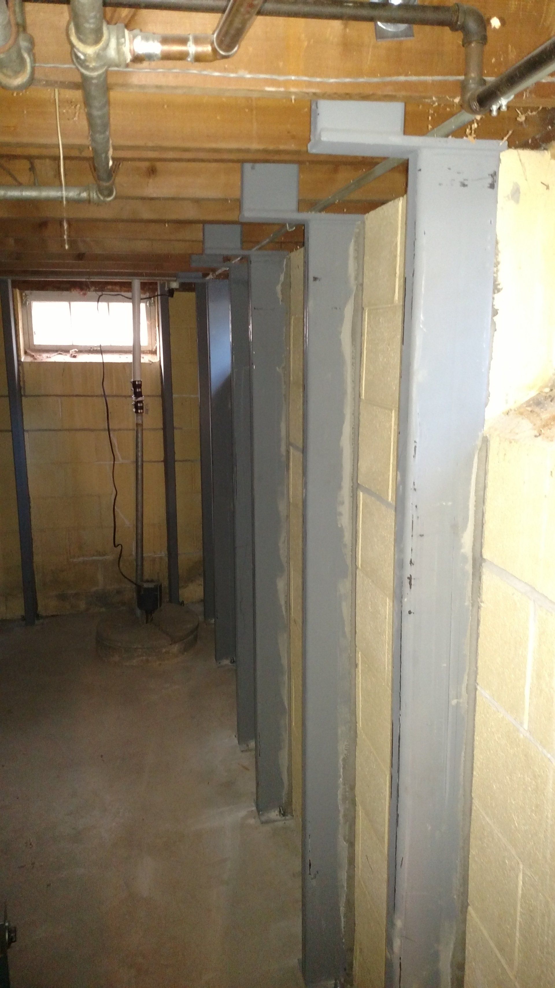 foundation waterproofing A basement with a lot of pipes and a window.