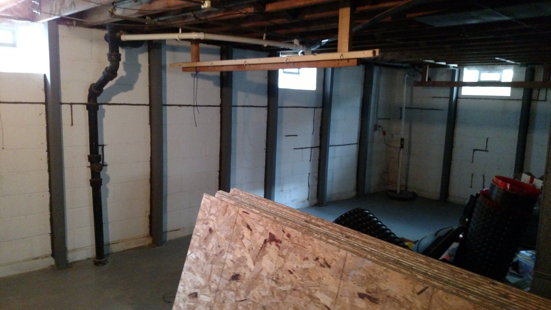 basement wall repair near me A basement with a large piece of plywood in the middle of it.