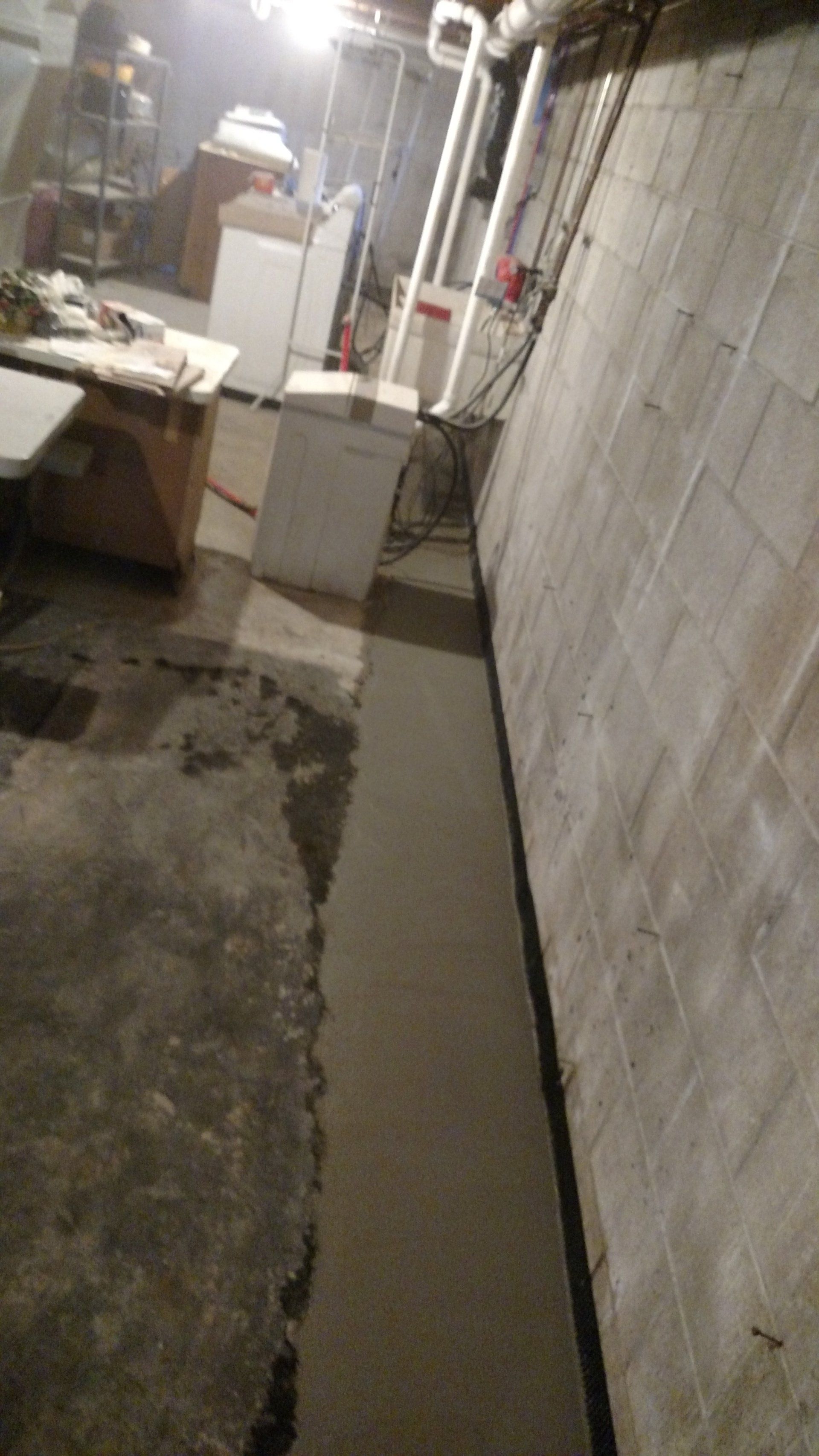 interior basement drainage system A basement with a concrete floor and a brick wall.