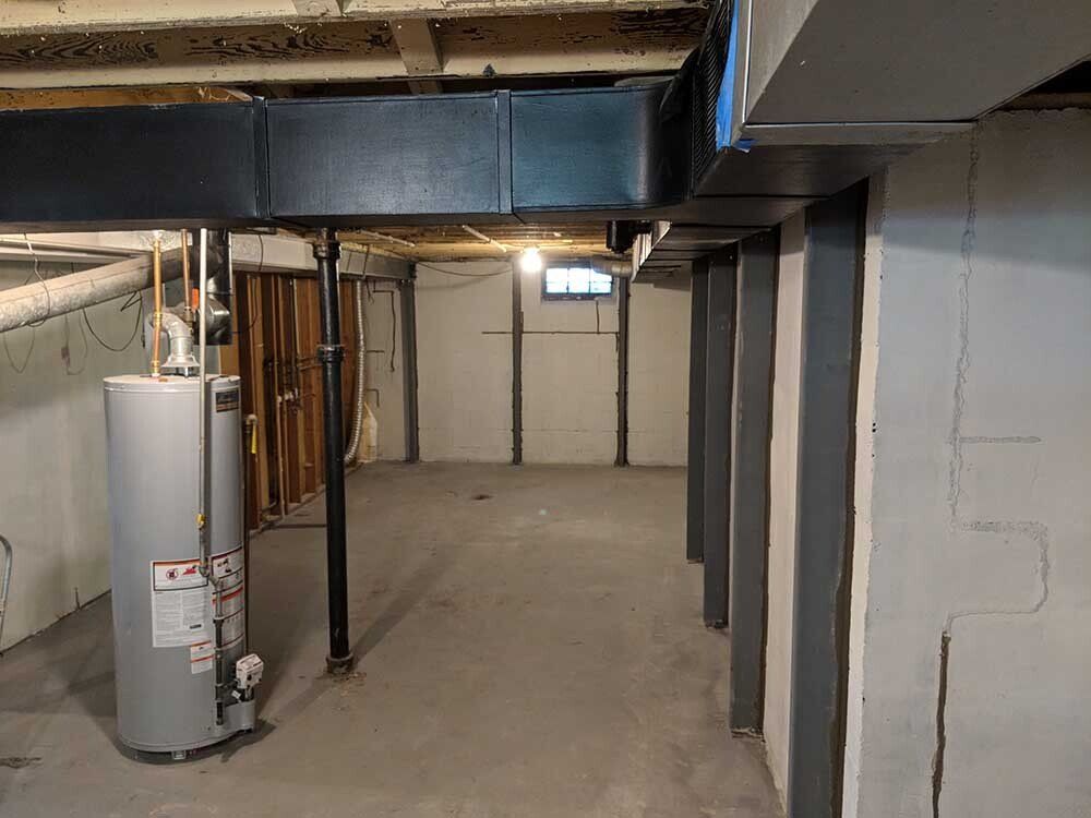 crack in basement wall An empty basement with a water heater and a window.