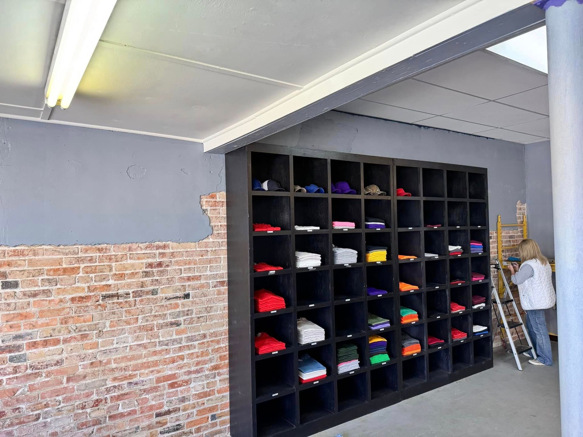 A woman is standing next to a ladder in a room with lots of shelves