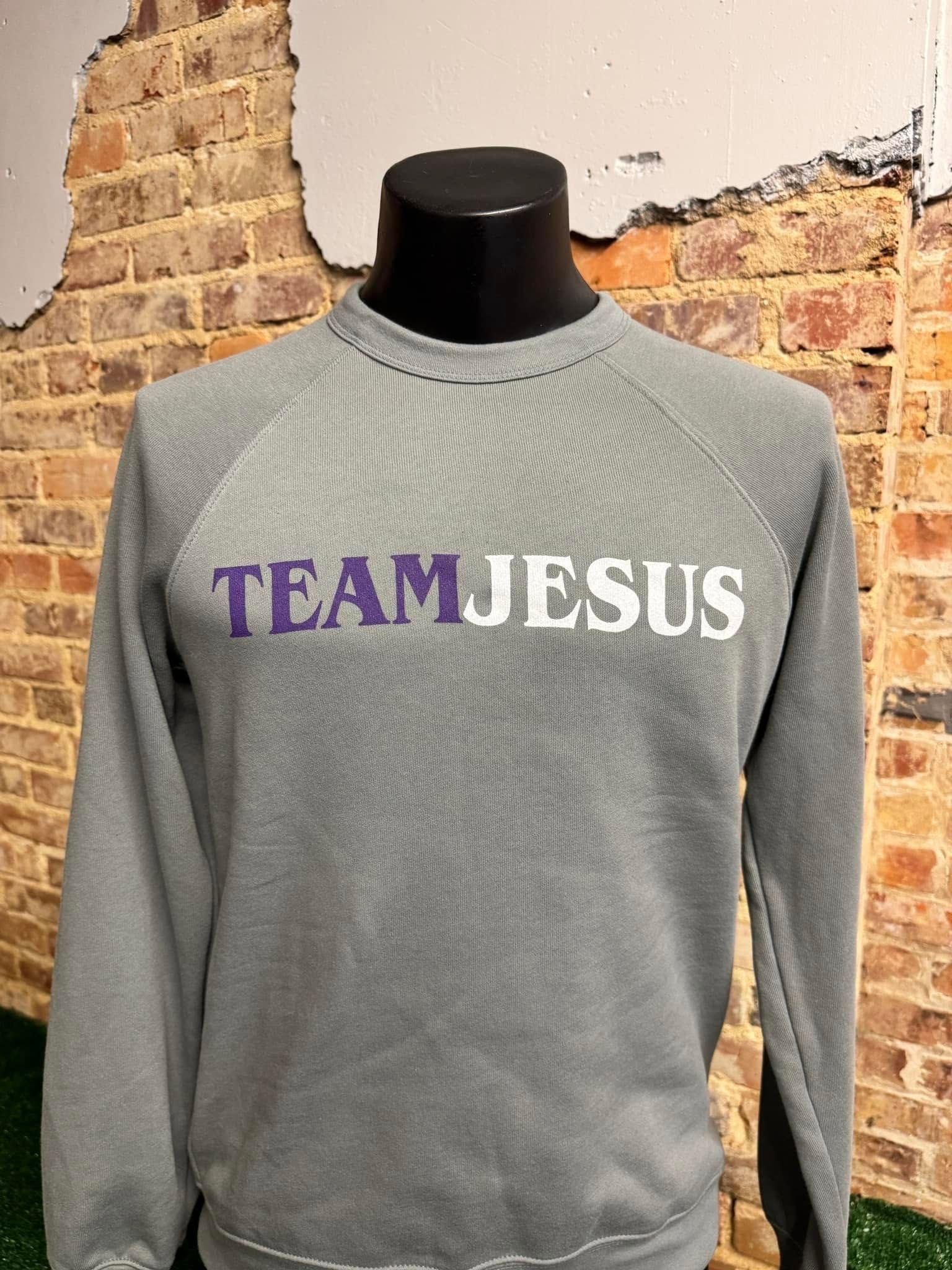 A grey sweatshirt with the words team jesus on it is on a mannequin in front of a brick wall.