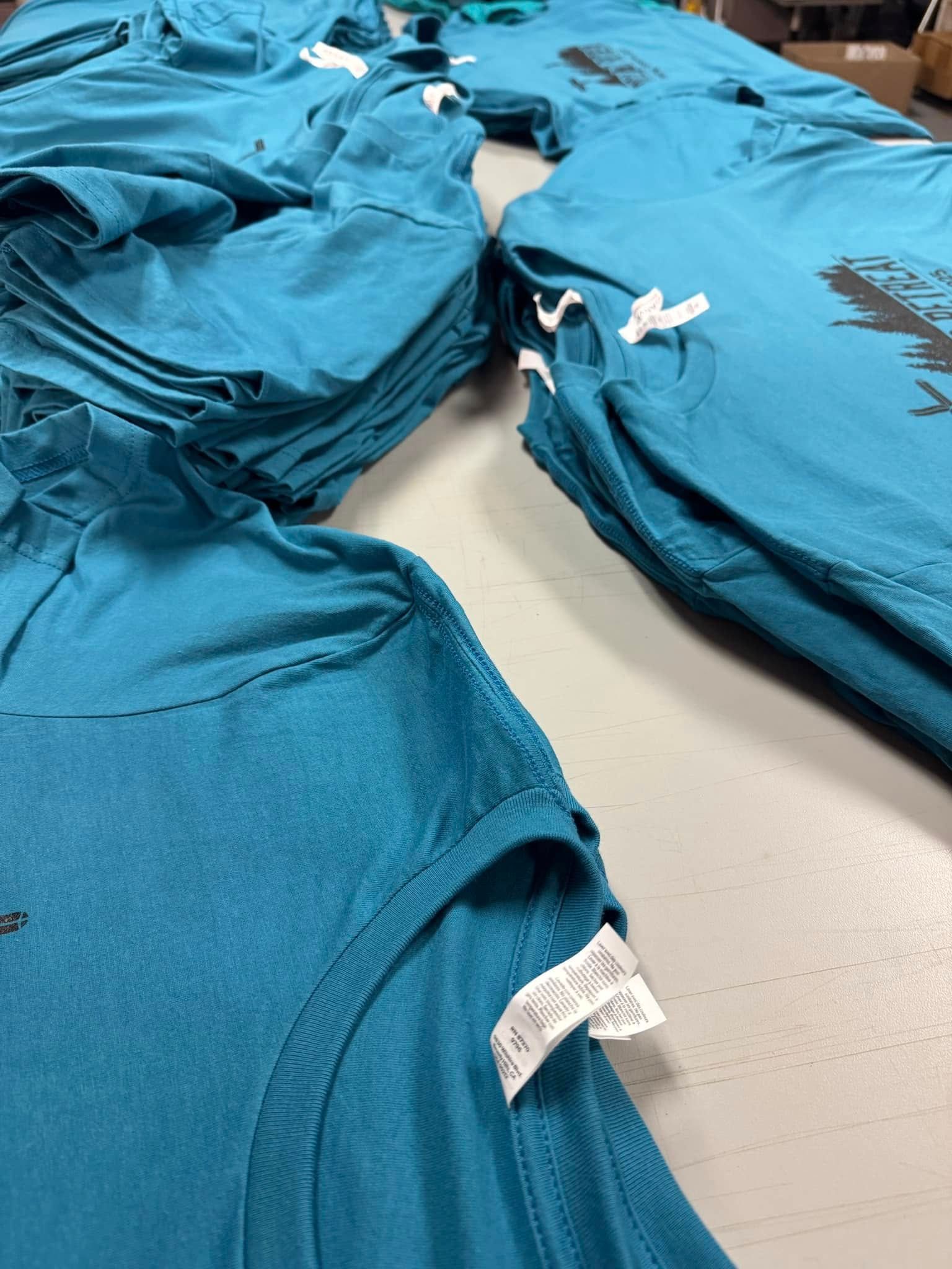 A bunch of blue shirts are stacked on top of each other on a table