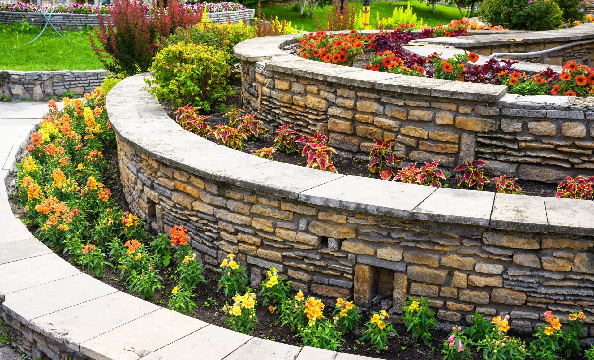 Curved stone garden wall with colorful flowers and white paving in a landscaped outdoor setting
