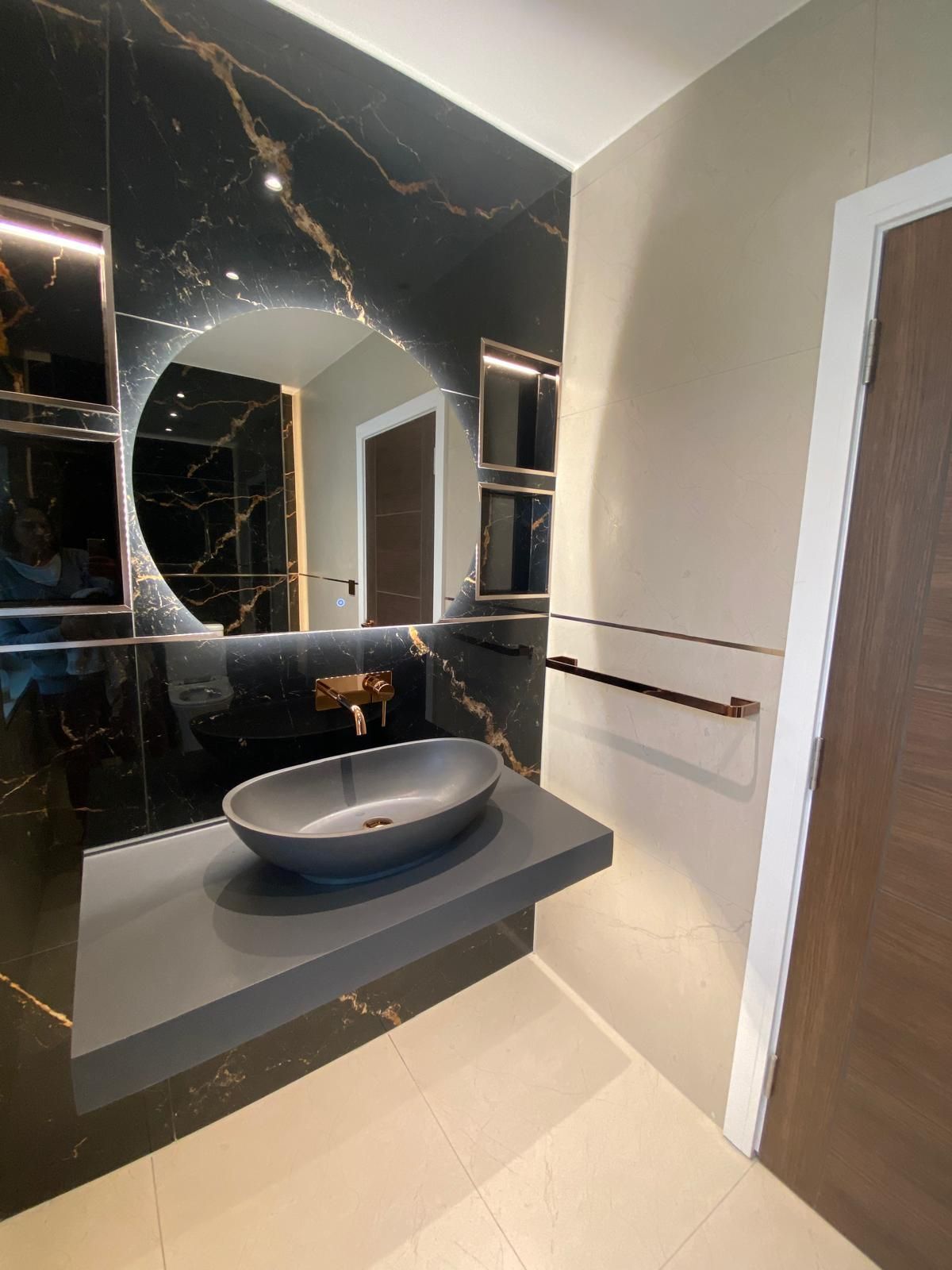 Modern bathroom vanity with black marble tile, wall mirror, vessel sink, and white towel bars.