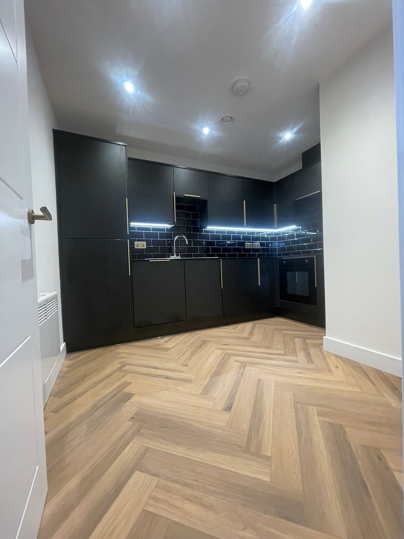 Modern kitchen with dark cabinets, black backsplash, and herringbone wood floor