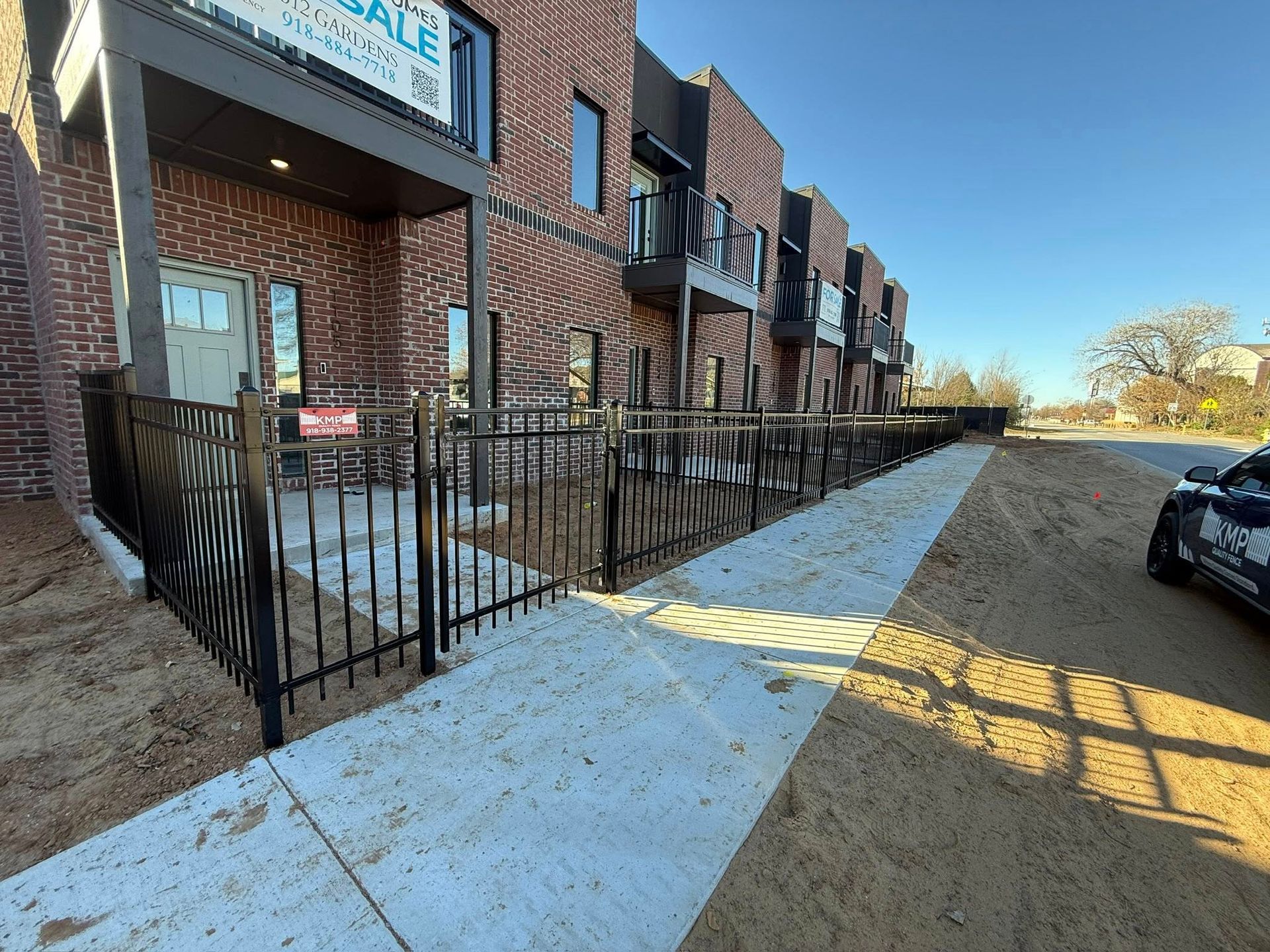 New brick townhomes with black fences and a concrete walkway under construction.