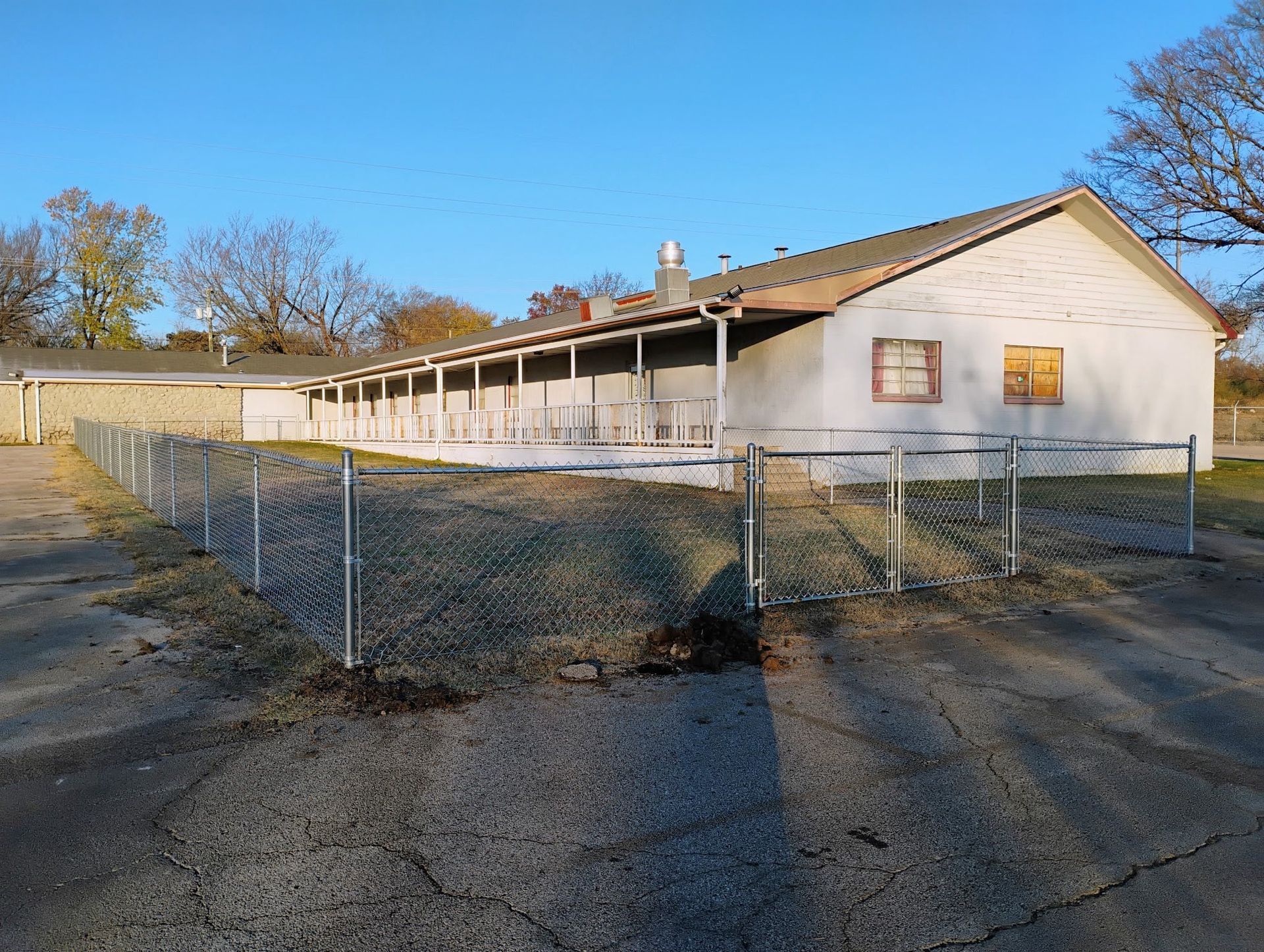 A one-story building with a porch, surrounded by a chain-link fence, on a clear day.