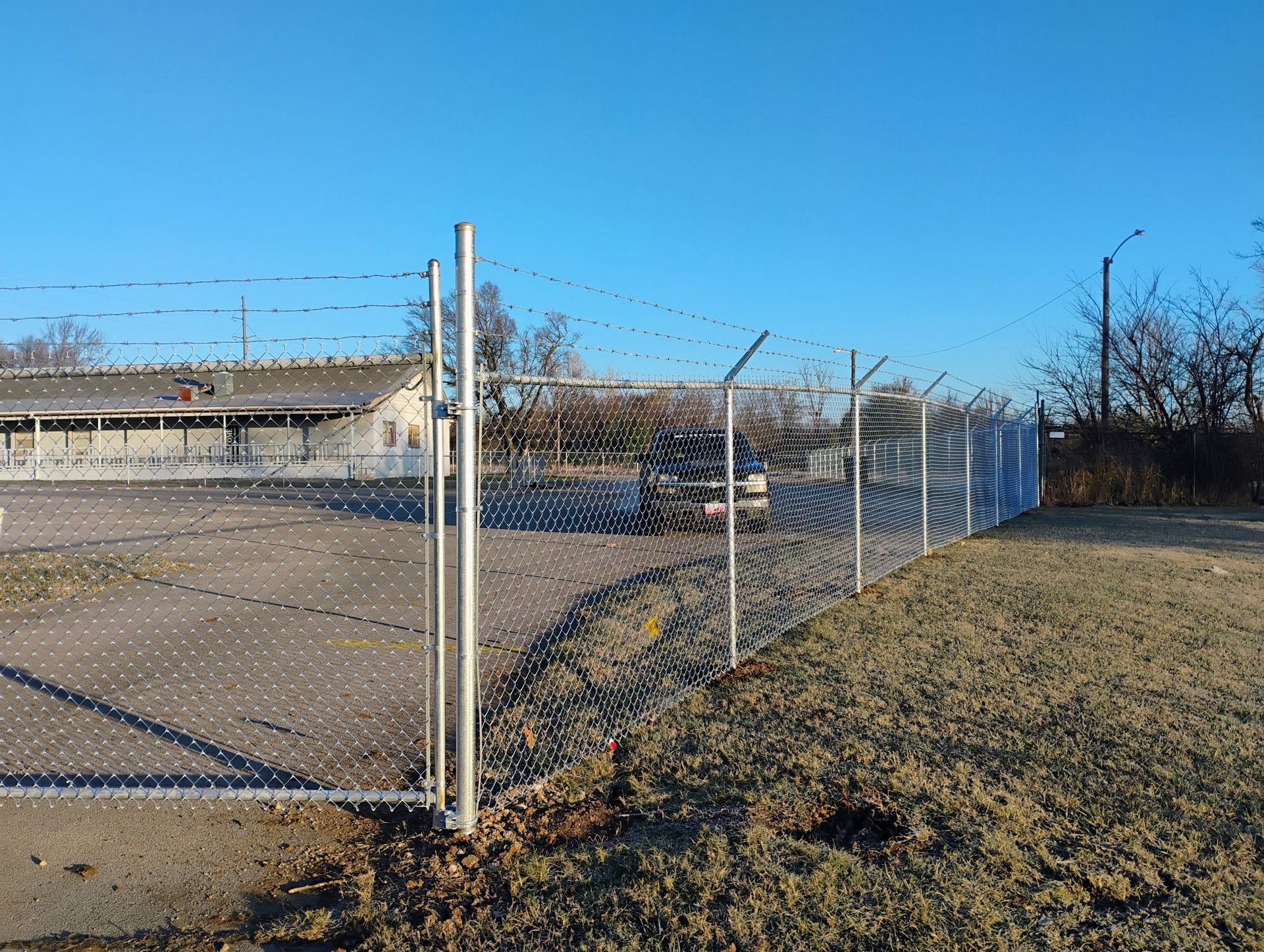 Chain-link fence with barbed wire. Building and grass in the background under a blue sky.