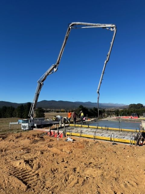 A concrete mixer truck with a crane attached to it is parked in front of a building under construction.