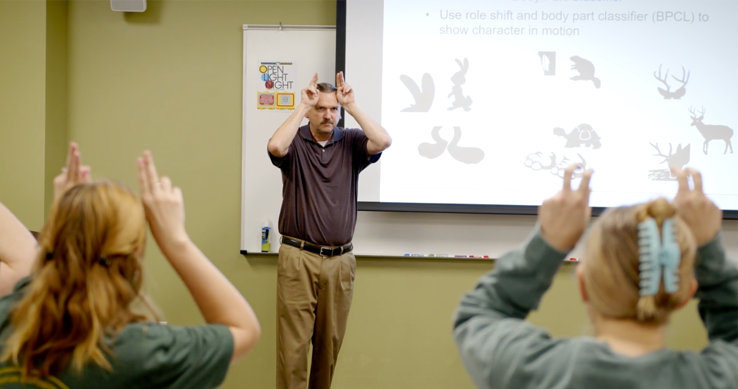 A woman is giving a presentation to a group of people sitting at a table.