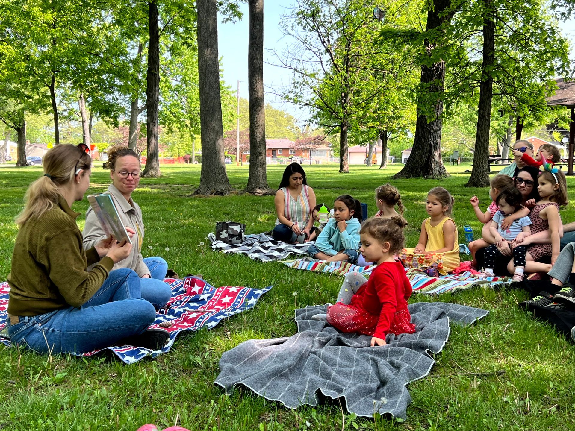 A group of people are sitting on blankets in a park.