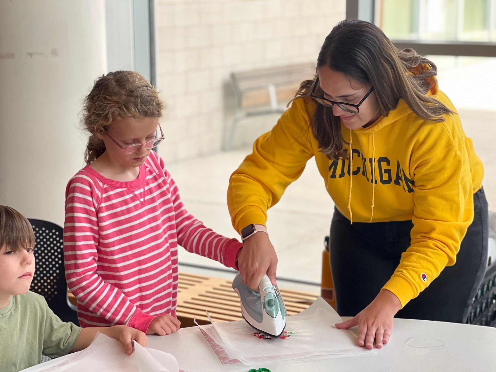 A woman in a yellow michigan sweatshirt is ironing a piece of fabric.