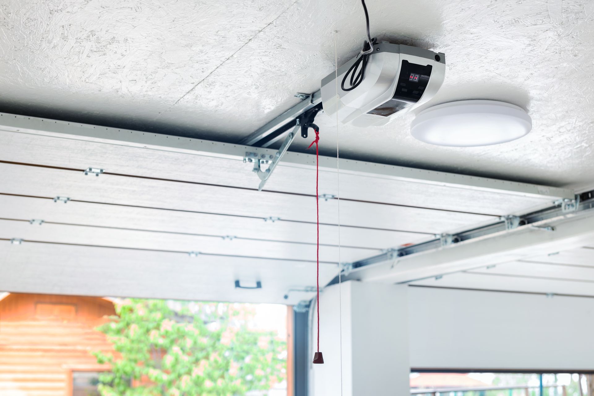 Garage door opener mounted on ceiling with red pull cord and metal rails