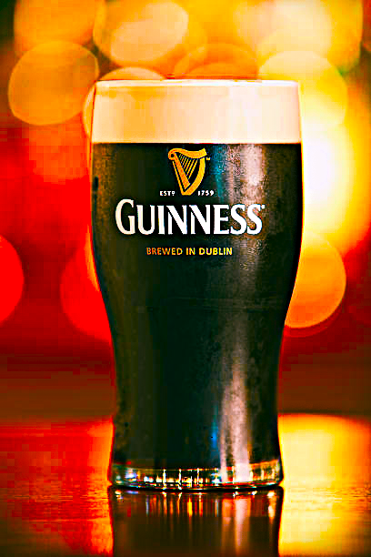 Pint of Guinness stout in a branded glass, with a creamy head. Dark liquid, blurred background.